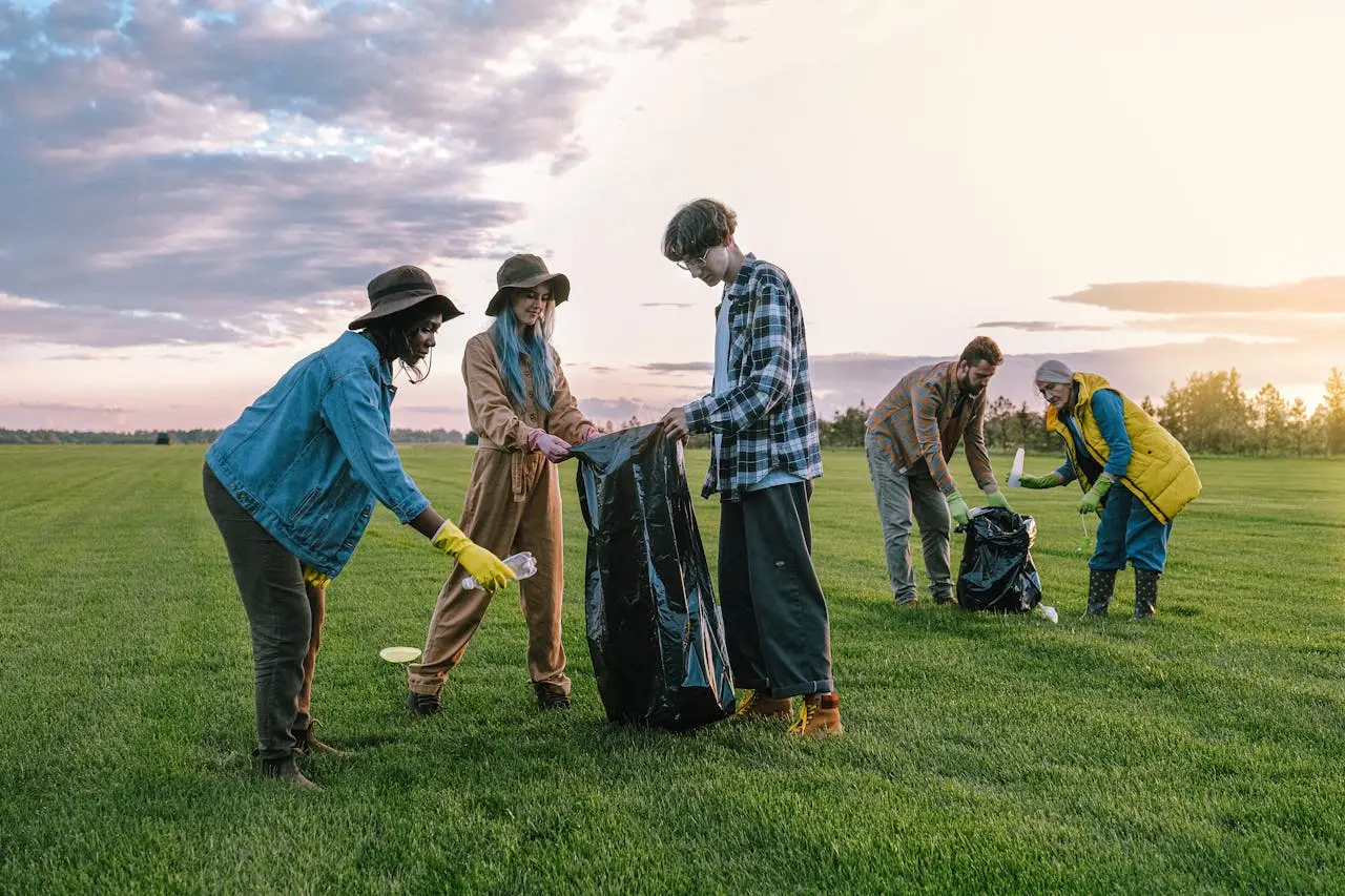 A diverse group of volunteers collecting trash in a field at sunset, promoting environmental awareness.